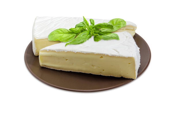 Dos trozos de queso brie en forma de sectores decorados con ramita de albahaca en el plato marrón sobre un fondo blanco
 - Foto, imagen