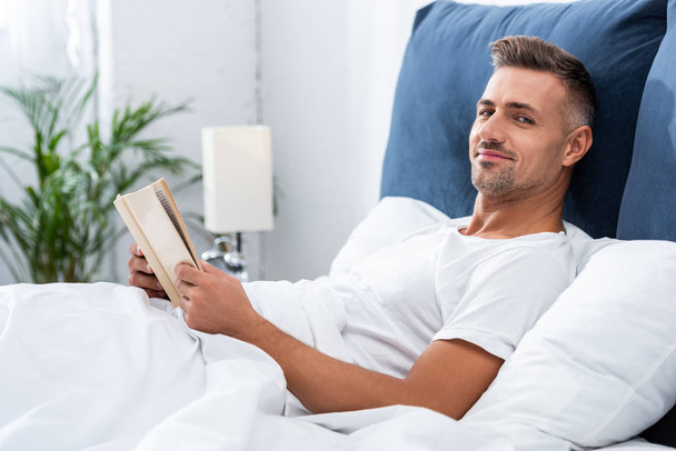 homem feliz lendo livro enquanto deitado na cama durante o tempo da manhã em casa
 - Foto, Imagem