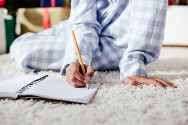 image recadrée d'un enfant afro-américain en pyjama écrivant quelque chose dans un carnet avec un crayon à la maison
 - Photo, image