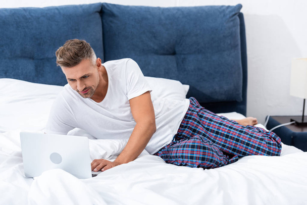 boldog felnőtt férfi szabadúszó szóló ágyban, és használ a laptop otthon reggel időszakban - Fotó, kép