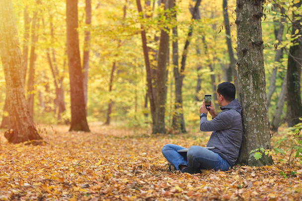 Man taking pictures with smartphone in forest, autumn colors, sunset warm light - Foto, afbeelding