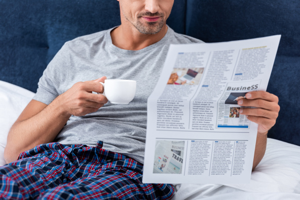 обрезанный образ бизнесмена с чашкой кофе чтение бизнес-газеты в постели дома
 - Фото, изображение