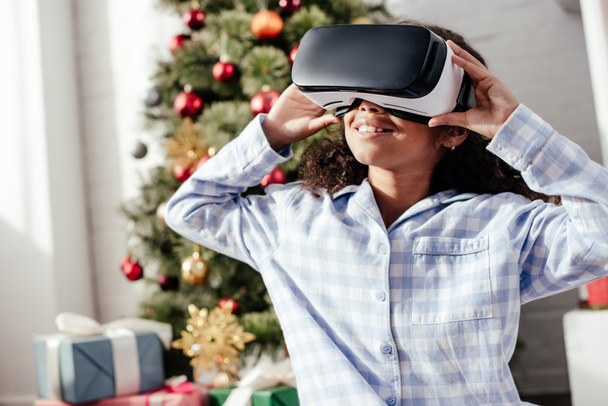 cheerful african american child in pajamas using virtual reality headset at home, christmas concept - Fotoğraf, Görsel