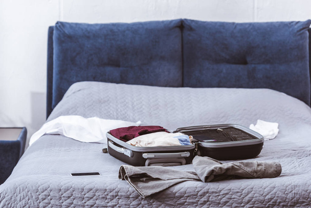 Selektywny fokus torby podróżnej, ubrań i smartphone na łóżko w domu  - Zdjęcie, obraz
