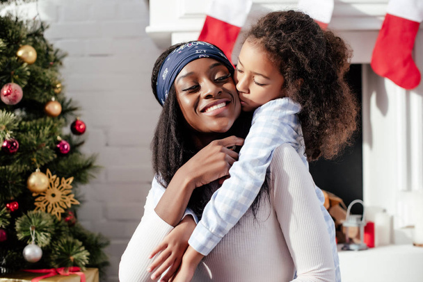 adorable african american daughter kissing mother at home, christmas concept - Φωτογραφία, εικόνα
