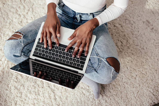 image recadrée de femme afro-américaine en utilisant un ordinateur portable sur le sol à la maison
 - Photo, image