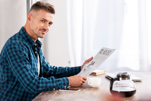 Veselý člověk sedí u stolu a čtenářský deník cestování v kuchyni doma - Fotografie, Obrázek