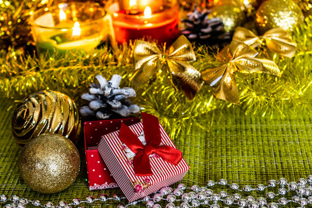 Colorful small gift boxes with gifts among Christmas tinsel and shiny toys and decorations. Winter and holiday scenery by the light of candles. - Photo, Image