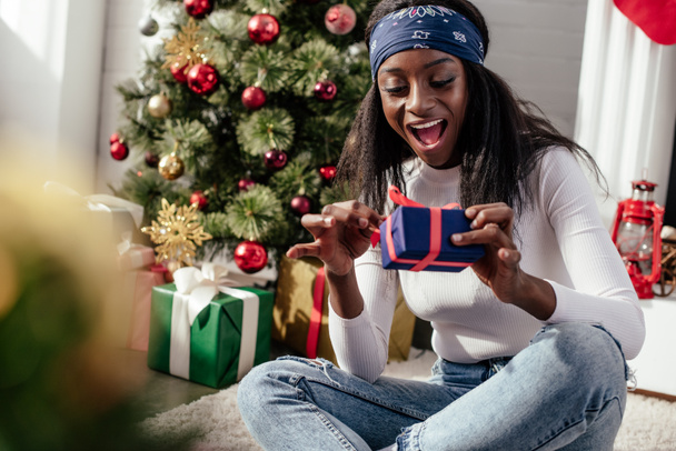 emocionado atractiva mujer afroamericana apertura de la caja de regalo de Navidad en casa
 - Foto, Imagen