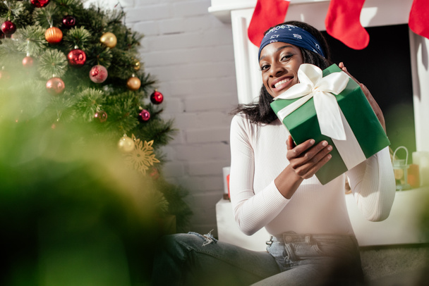 興奮した魅力的なアフリカ系アメリカ人女性家でクリスマス プレゼントを抱えて、カメラ目線 - 写真・画像