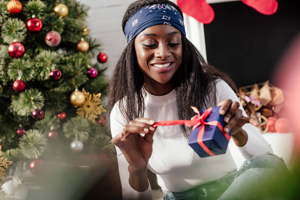 Selektivní fokus usmívající se atraktivní afroamerické ženy doma otevření vánoční dárek - Fotografie, Obrázek