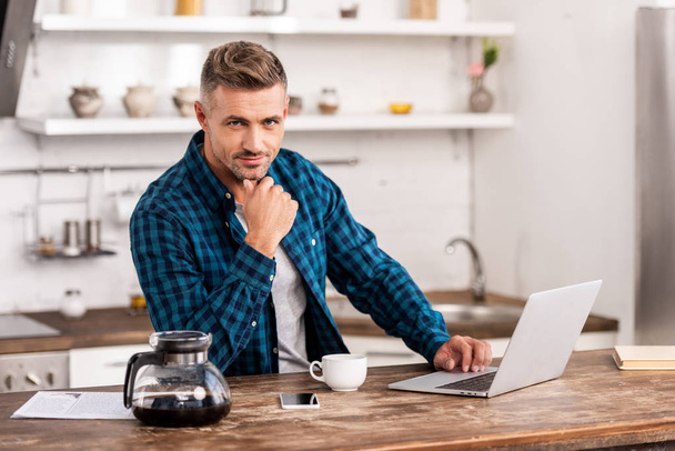 handsome man in checkered shirt using laptop and looking at camera - Φωτογραφία, εικόνα