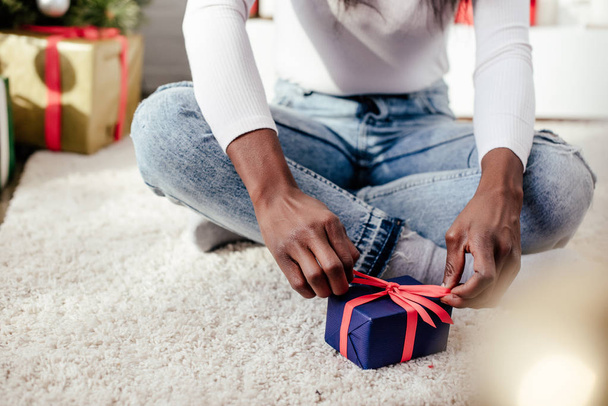 cropped image of african american woman tying christmas gift at home - Фото, зображення