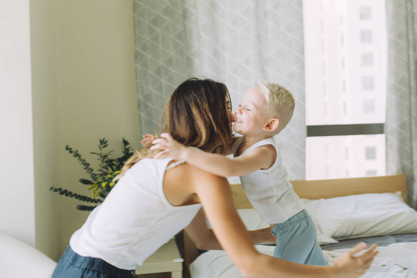 young beautiful mother having fun with her son in bedroom at home - Photo, Image