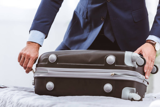 cropped shot of businessman in suit packing suitcase on bed - Foto, Imagen