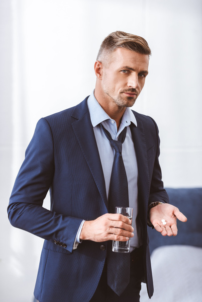 businessman in suit holding glass of water with pills and looking at camera - Foto, Imagem
