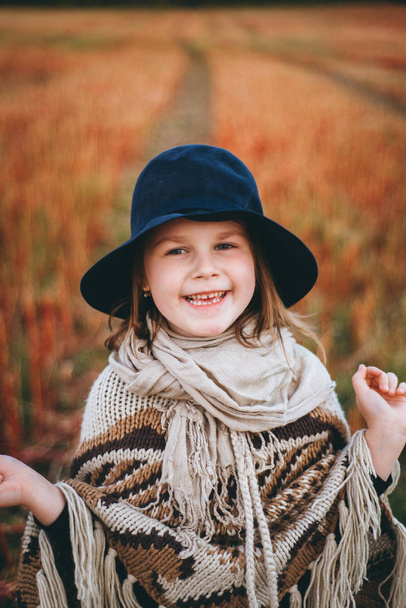 Portrait of smiling girl in poncho and hat walking by autumnal field - Foto, immagini