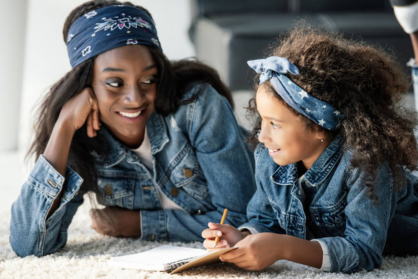 retrato de mulher afro-americana sorrindo ajudando filha fazendo lição de casa em casa
 - Foto, Imagem