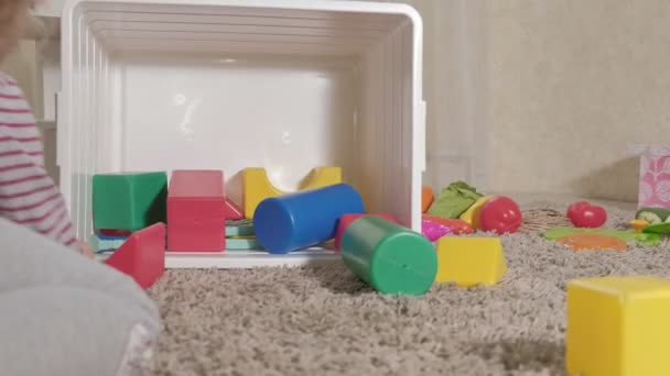 Güzel gülüyor küçük çocuk, okul öncesi sarışın, oda katta oturan beyaz kutu içinde renkli oyuncaklar ile oynama - Video, Çekim