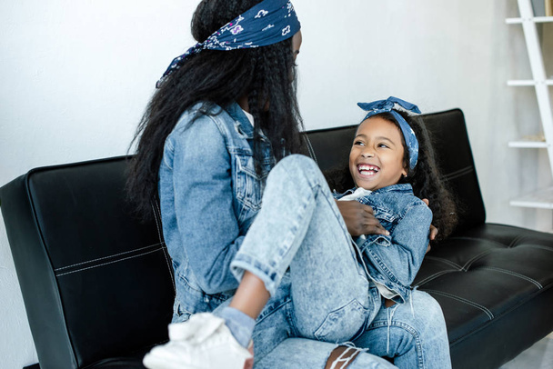 african american woman and cheerful daughter having fun on sofa at home - Foto, afbeelding
