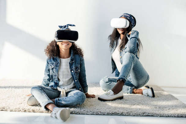 smiling african american mother and daughter in similar clothing and vr headsets at home - Foto, Bild