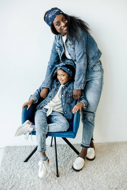 sorridente afro-americana mãe perto filha na cadeira em casa
 - Foto, Imagem