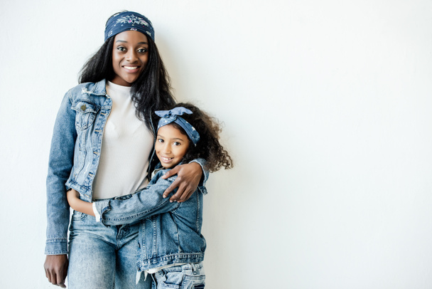 portrait of stylish african american mother and daughter in similar clothing posing at wall at home - Photo, Image