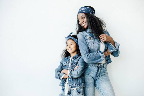 stylish african american mother and daughter in similar clothing posing at wall at home - Zdjęcie, obraz