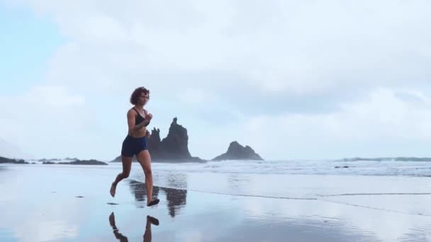 Aktív sportos nő szaladni ocean surf víz medence tartani fit és egészség. Naplemente fekete homokos strand háttér nap. Női fitness, futás képzés és sport tevékenység a családi nyaralás. - Felvétel, videó
