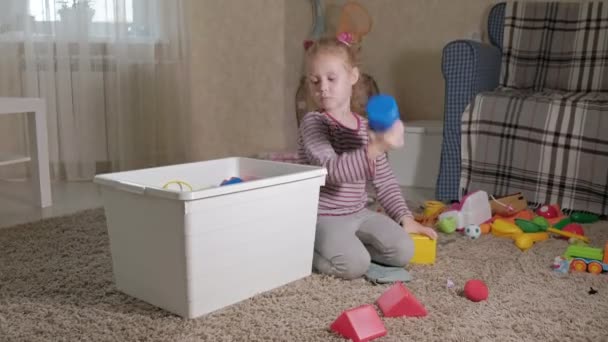 Πολυ γέλιο μικρό παιδί, προσχολική Ξανθιά, παίζει με τα πολύχρωμα παιχνίδια σε ένα άσπρο κιβώτιο, κάθεται στο πάτωμα στο δωμάτιο - Πλάνα, βίντεο