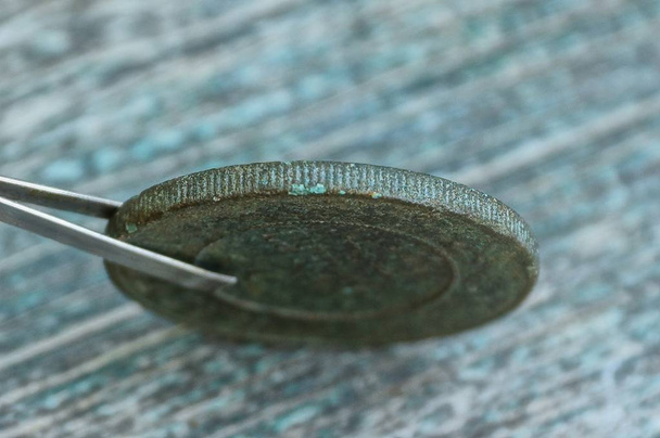 пинцет с металлической монетой из ретро-меди на столе
 - Фото, изображение