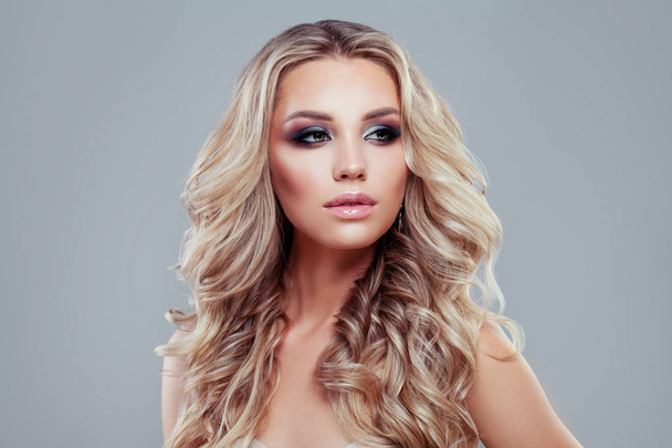 Blonde beauty. Young perfect woman with long curly hair and makeup on blue background - Φωτογραφία, εικόνα