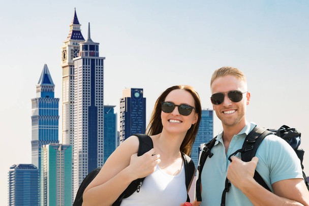 Portrait Of A Smiling Young Couple Wearing Sunglasses In City - Foto, imagen