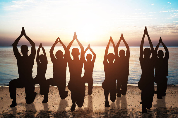 Silueta de personas haciendo yoga en la playa de arena al atardecer
 - Foto, Imagen