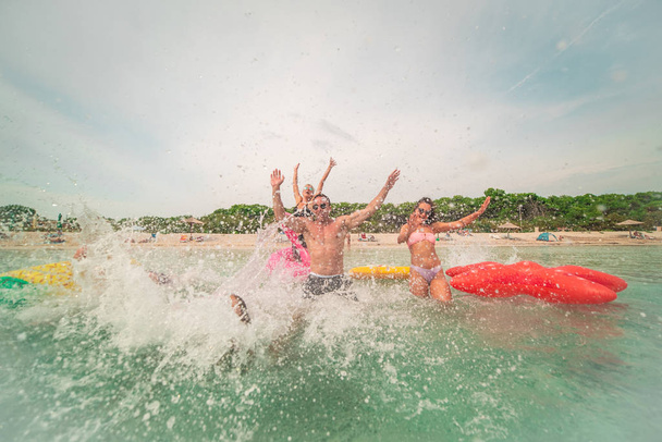 Groupe d'amis de la famille courant follement dans la mer avec des matelas gonflables sur la plage d'été
. - Photo, image