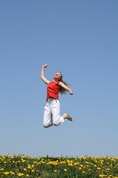 Hymyilevä onnellinen tyttö hyppää kukinnan alalla
 - Valokuva, kuva