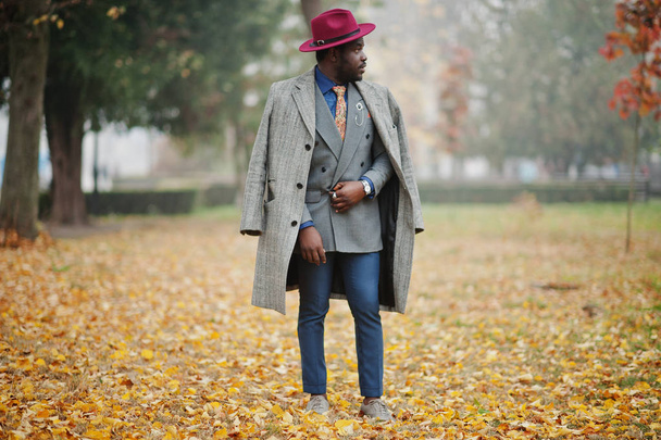 Elegante modello di uomo afroamericano in cappotto grigio, cravatta giacca e cappello rosso posato in strada nebbioso tempo in autunno
. - Foto, immagini