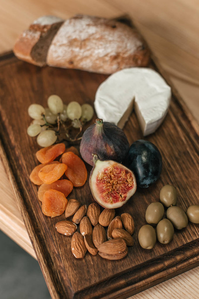 Dřevěná deska s ovocem, sýrem a ořechy - Fotografie, Obrázek