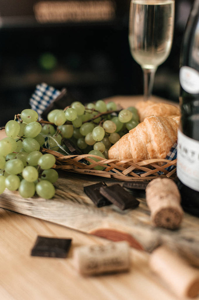 Weinflasche, grüne Trauben, Schokoladenstücke und Croissants auf Holzbrett - Foto, Bild