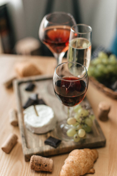 Glasses with red and white wine on wooden board with grapes, cheese and chocolate - Foto, Bild