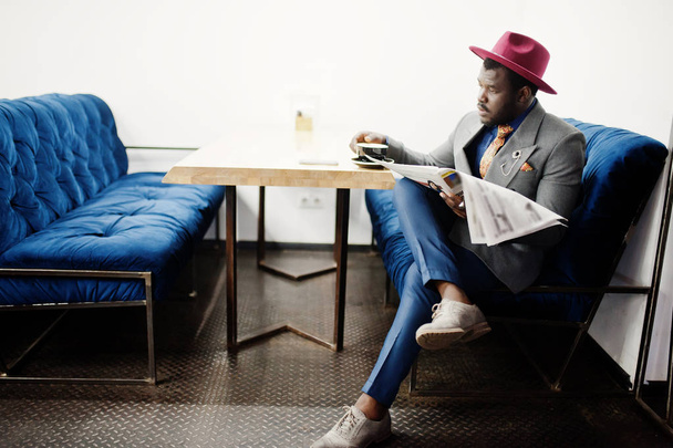 Stylish African American man model in gray jacket tie and red hat drink coffee at cafe and read newspapers. - Foto, Bild