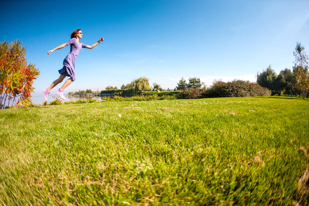 Une fille en robe court dans une prairie verte. Femme marchant dans le parc. Activité dans la nature. Mince brune s'amuse
. - Photo, image