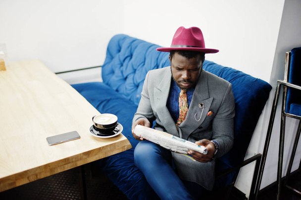 Stylish African American man model in gray jacket tie and red hat drink coffee at cafe and read newspapers. - Φωτογραφία, εικόνα