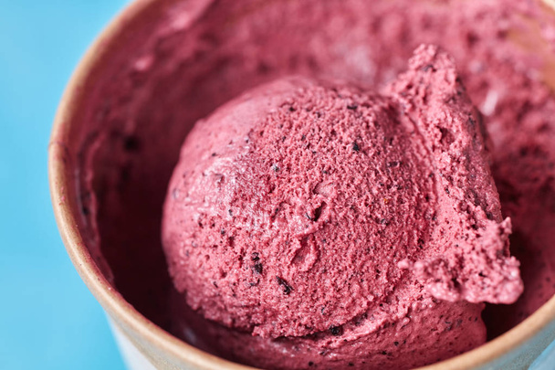 A scoop of healthy homemade berry ice cream in a paper cup on a blue background macro photo. Top view - Fotografie, Obrázek