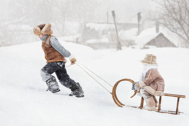 Δύο παιδιά με έλκηθρο με βουνό ζεστή μέρα του χειμώνα - Φωτογραφία, εικόνα