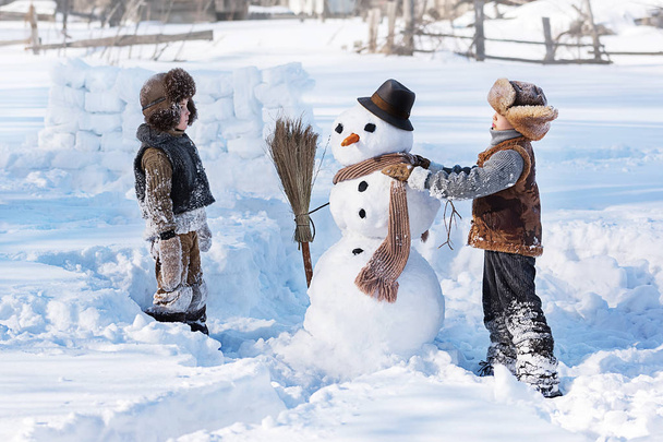 Two little boys sculpt a snowman in the backyard of the house clear winter day - Fotoğraf, Görsel