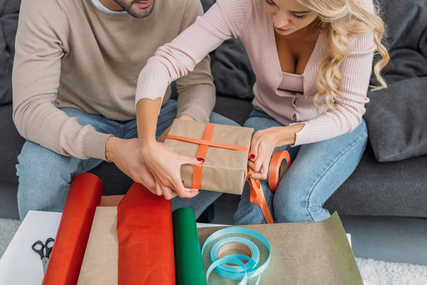 cropped image of couple wrapping christmas gift box together at home - Foto, Imagen