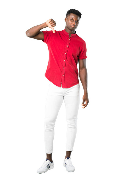 Nuoren afrikkalaisen miehen kokovartalo osoittaa peukalon alaspäin negatiivisella ilmeellä. Surullinen ilme valkoisella taustalla
 - Valokuva, kuva