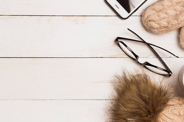 Düz lay kış sıcak giysiler, eldiven, gözlük ve smartphone kopya alanı ahşap beyaz zemin üzerine örme şapka ile. Noel kavramı - Fotoğraf, Görsel