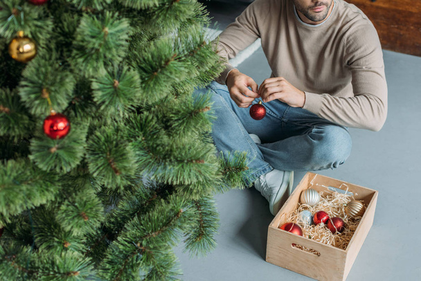 кадроване зображення людини, Прикраси Різдвяна ялинка з дрібнички і, сидячи на підлозі будинку - Фото, зображення